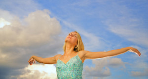 Beautiful blond girl with arms wide open over blue cloudy sky